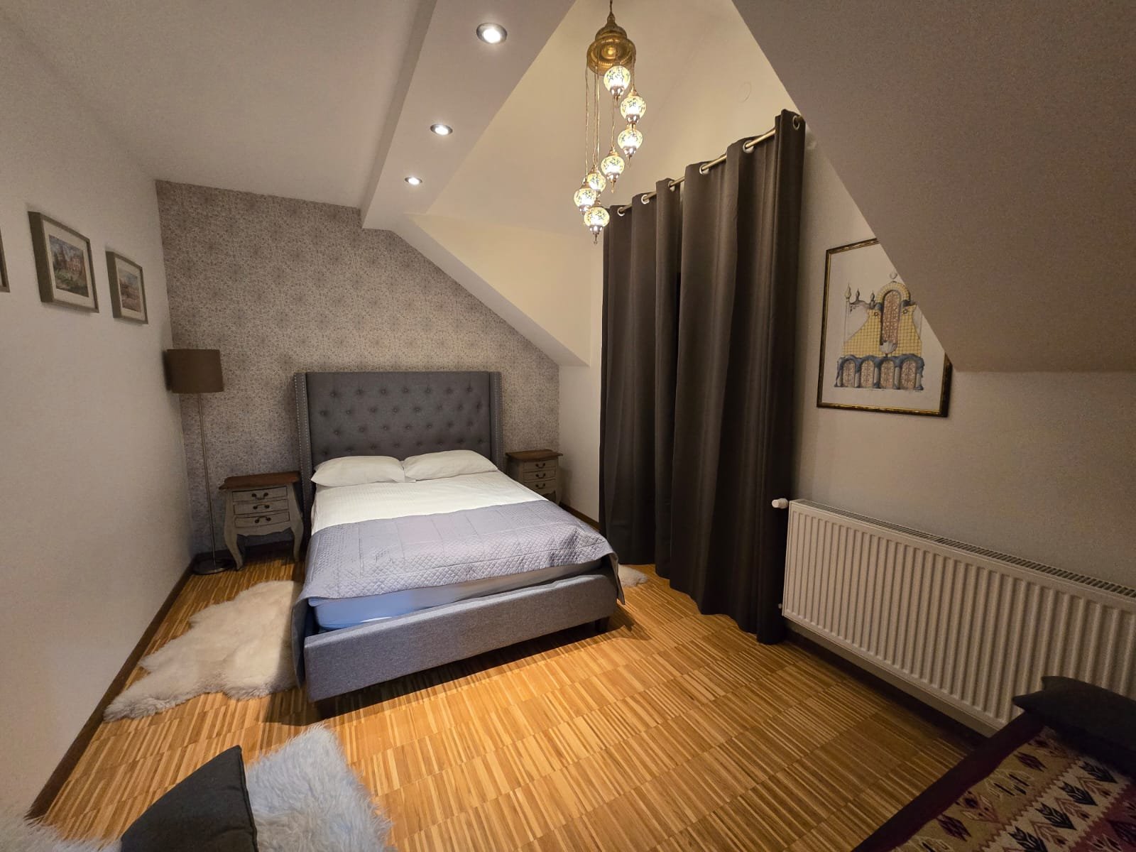 Pokój Queen z dużym łóżkiem, szarym zagłówkiem, żyrandolem i parkietem